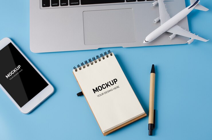 PSD travel booking with laptop, notebook, smartphone and airplane model on blue table.