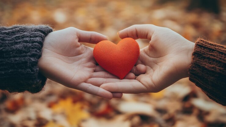 PSD two hands gently hold a small red heart outdoors in autumn