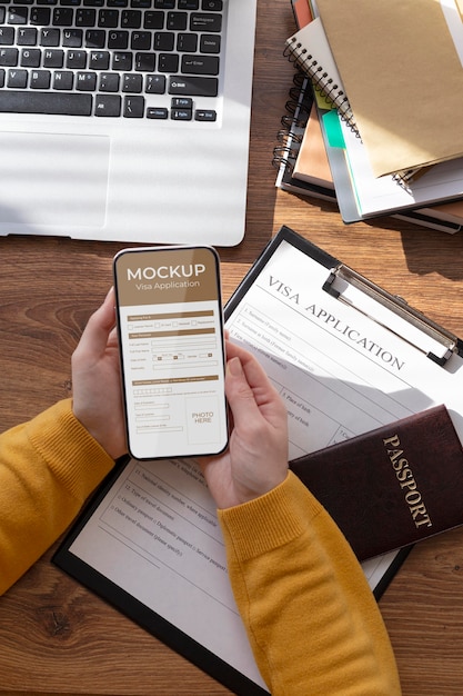 PSD visumaanvraag mock-up in smartphone vastgehouden door menselijke handen op bureau met paspoort, laptop en documenten