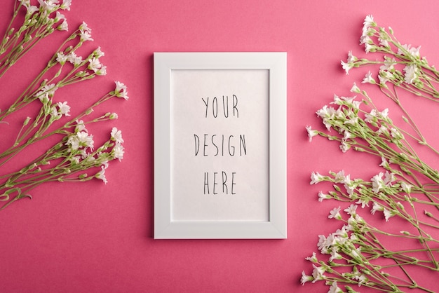 PSD white empty photo frame with flowers on pink table