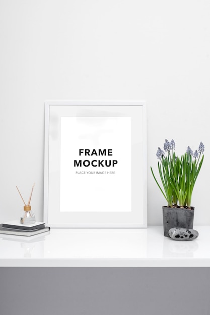 A white frame mockup on a white table next to a plant