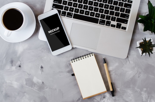 white smartphone with black blank screen on office desk with laptop and cup of coffee