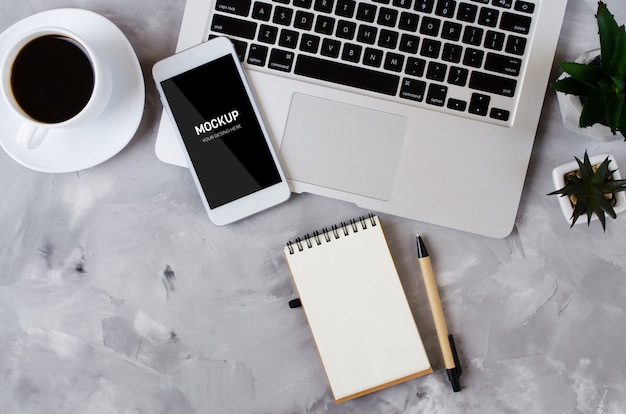 PSD white smartphone with black blank screen on office desk with laptop and cup of coffee