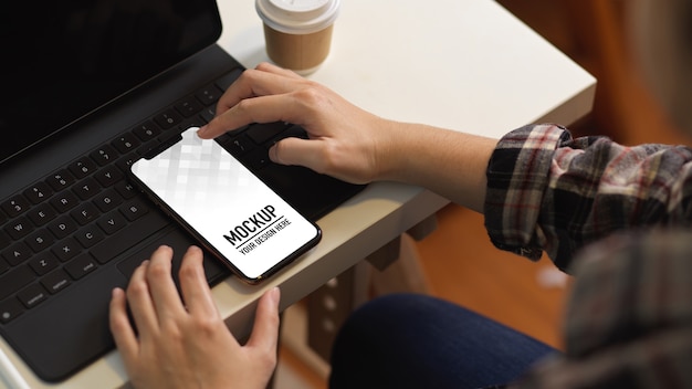 Widok z góry kobiecej dłoni dotykającej ekranu makiety smartfona na klawiaturze tabletu