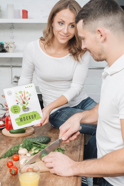 Woman holding book in the kitchen while man cooks