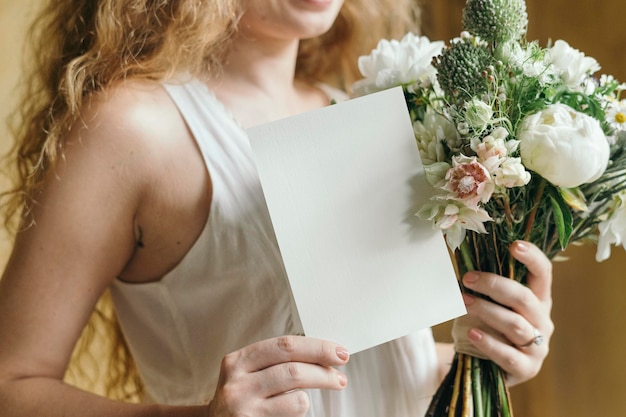 カードのモックアップと白い花の花束を保持している女性