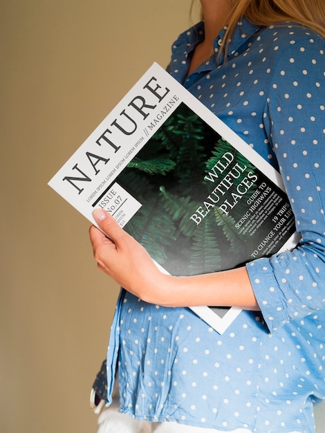 Женщина, держащая журнал о природе рядом с ее грудью