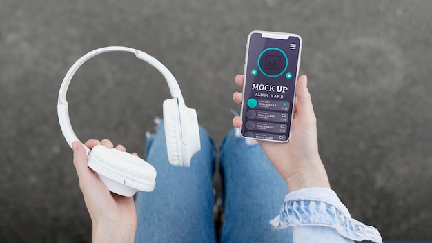 PSD woman holding phone with music app mock-up and headphones