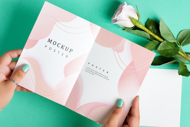 Woman's hands are holding empty mock-up paper brochure above rose