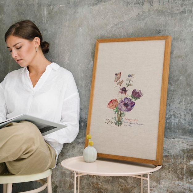 PSD woman sitting on a stool and reading a book by a photo frame