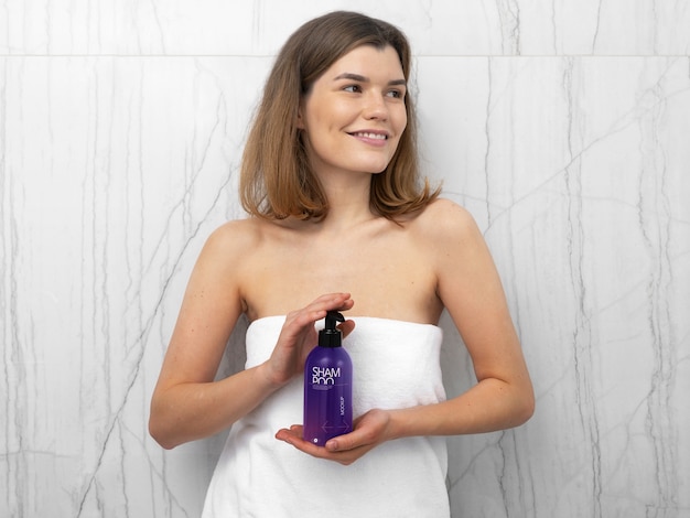 PSD woman in towel holding mock-up bottle of shampoo