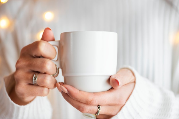 Donna in un maglione bianco con un mockup di tazza bianca