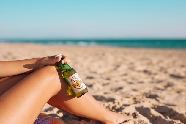 ビーチでビール瓶のモックアップを持つ女性