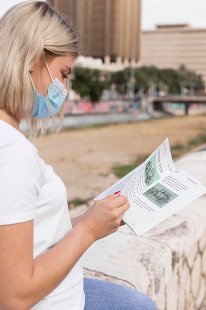 PSD woman with mask reading book on street