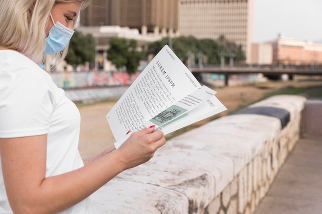 Woman with mask reading book on street