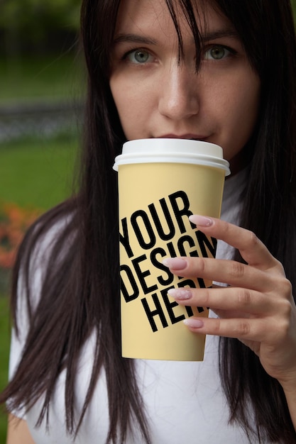 Ragazza gialla della tazza di caffè di carta grande che beve il mockup di colore mutevole del primo piano del caffè psd