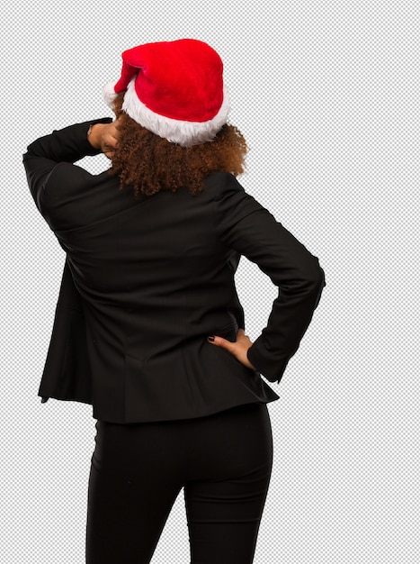 PSD young black businesswoman wearing a christmas santa hat from behind thinking about something