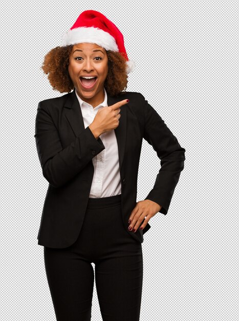 Young black businesswoman wearing a christmas santa hat smiling and pointing to the side