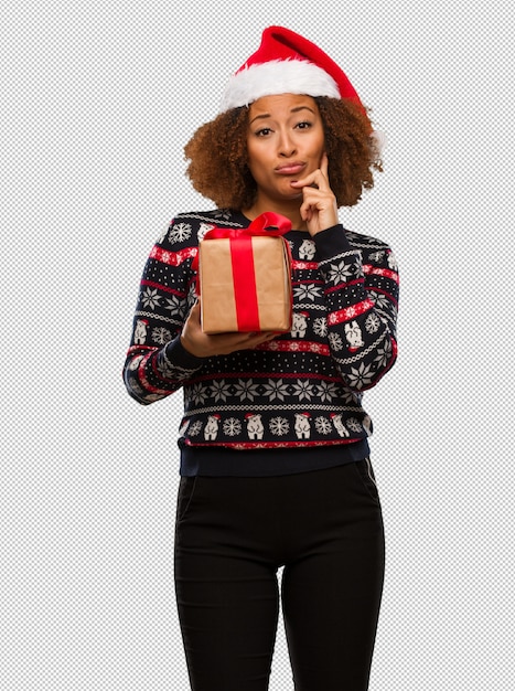 Young black woman holding a gift in christmas day doubting and confused