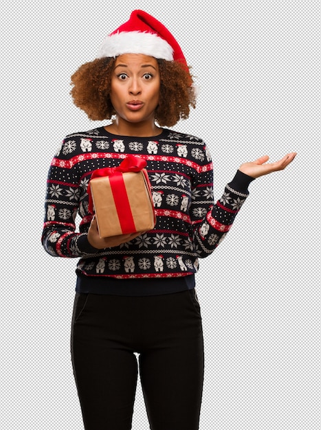 Young black woman holding a gift in christmas day holding something on palm hand