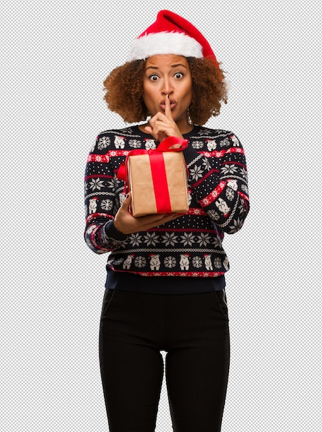 PSD young black woman holding a gift in christmas day keeping a secret or asking for silence