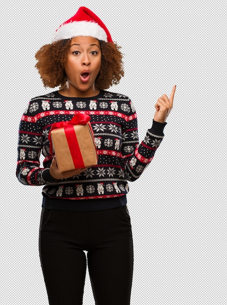 Young black woman holding a gift in christmas day pointing to the side