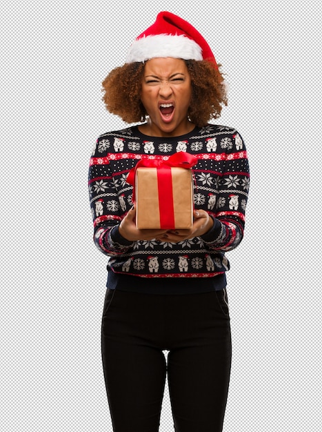 PSD young black woman holding a gift in christmas day screaming very angry and aggressive