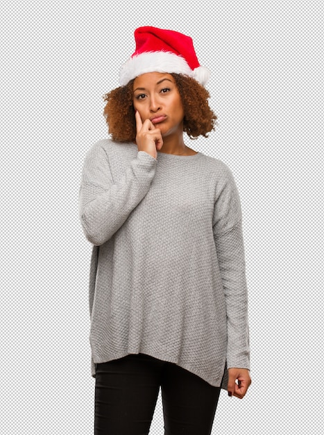 Young black woman wearing a santa hat doubting and confused