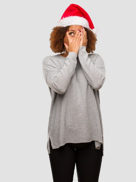 Young black woman wearing a santa hat feels worried and scared