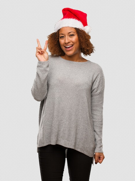 Young black woman wearing a santa hat fun and happy doing a gesture of victory