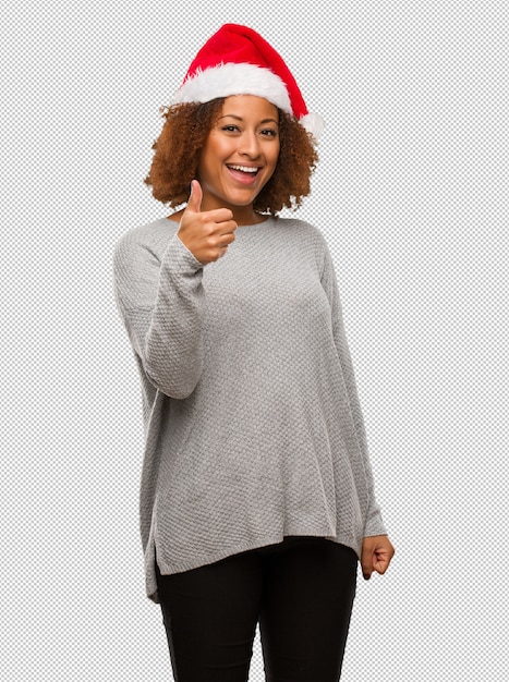 Young black woman wearing a santa hat smiling and raising thumb up