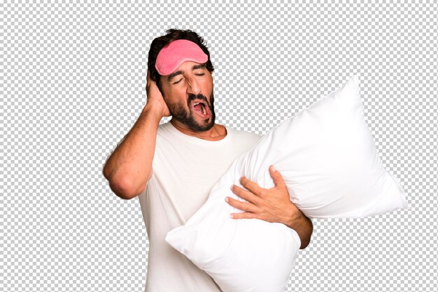 Young crazy bearded and expressive man wearing pajamas and eye mask and with a pillow