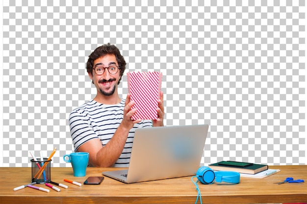PSD giovane grafico pazzo su una scrivania con un computer portatile e con un secchio di pop corn