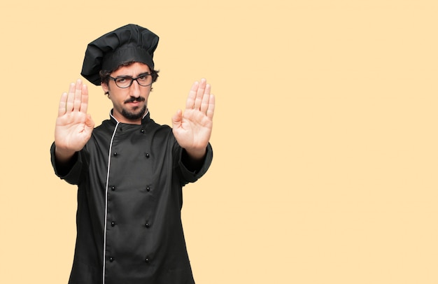 Young crazy man as a chef signaling stop with both palms of hands facing forward