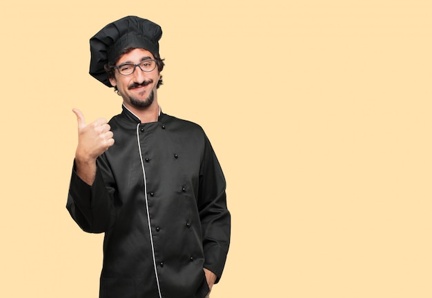 Young crazy man as a chef with a satisfied, proud and happy look with thumbs up