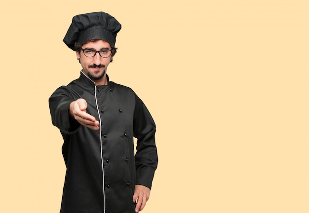 young crazy man as a chef with a serious, confident, proud and stern expression offering a handshake