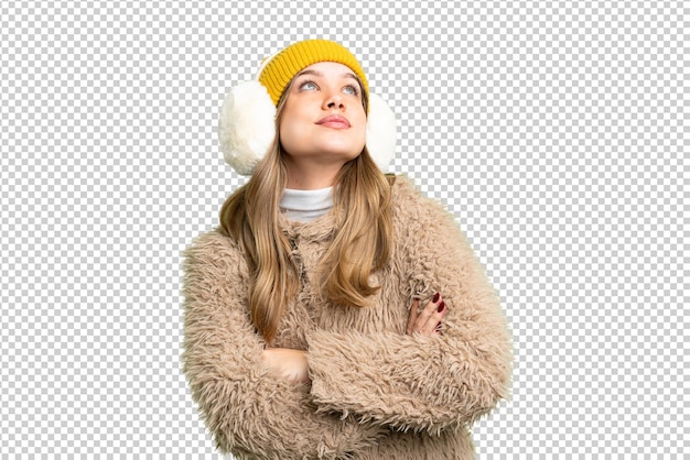young girl wearing winter muffs over isolated chroma key background looking up while smiling