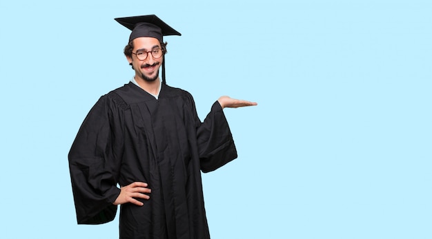 PSD young graduated man smiling with a satisfied expression showing an object or concept with one hand