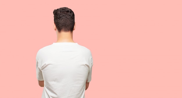 young handsome man giving back to the camera, standing with arms crossed