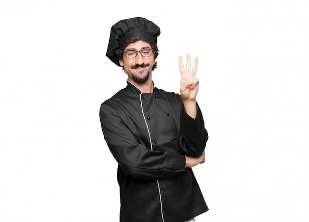 шеф-повар молодой человек улыбается и выглядит удовлетворенным и счастливым, считая номер три пальцами