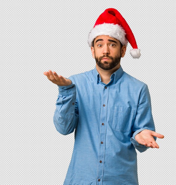 Young man wearing santa hat confused and doubtful