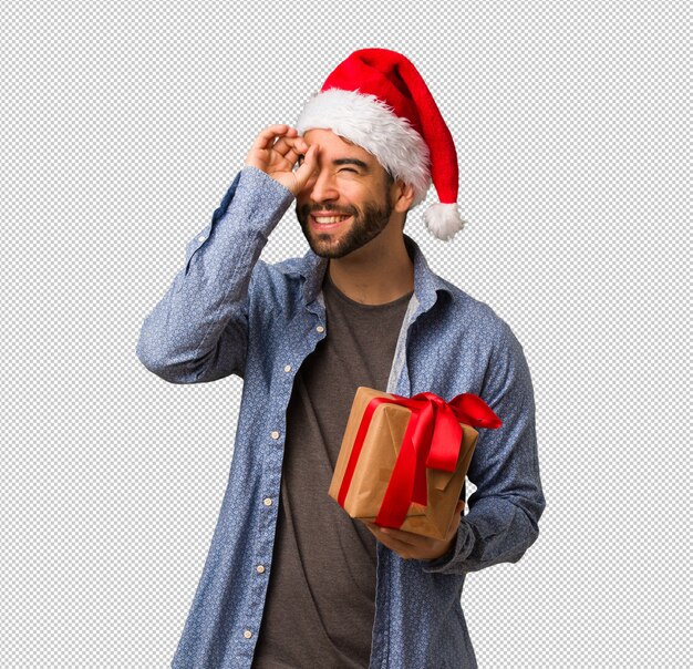 Young man wearing santa hat making the gesture of a spyglass