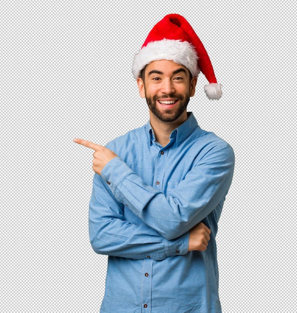 손가락으로 측면을 가리키는 산타 모자를 쓰고 젊은 남자