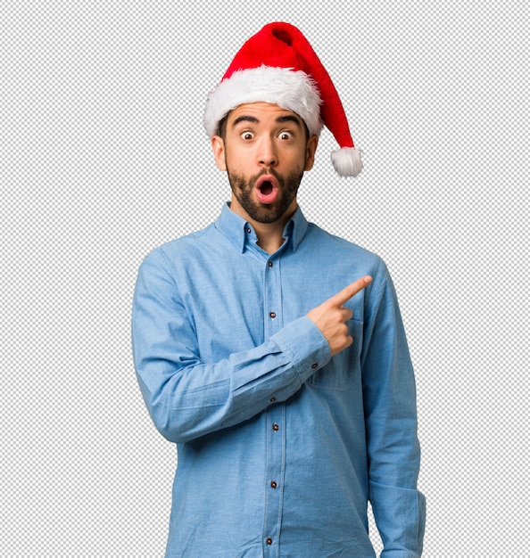 Young man wearing santa hat pointing to the side