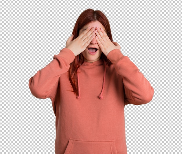 Young redhead girl with pink sweatshirt covering eyes by hands