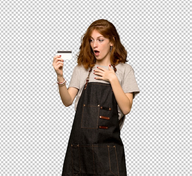 young redhead woman with apron holding a credit card and surprised