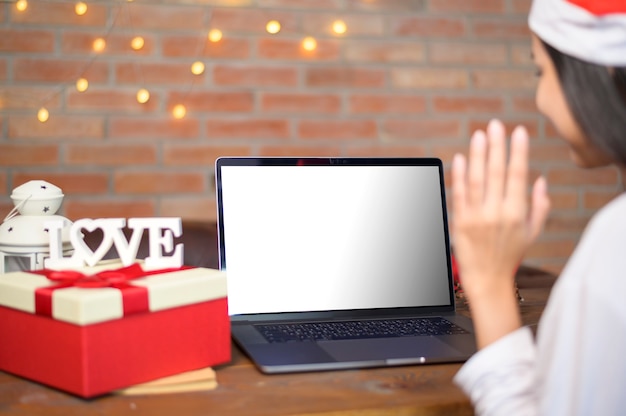 Young smiling woman wearing red santa claus hat making video call on laptop mockup