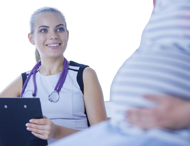 Young woman doctor with stethoscope and tablet speaking with pregnant woman at hospital