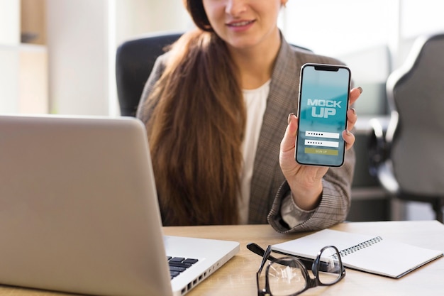 Young woman showing her phone screen mock-up at work