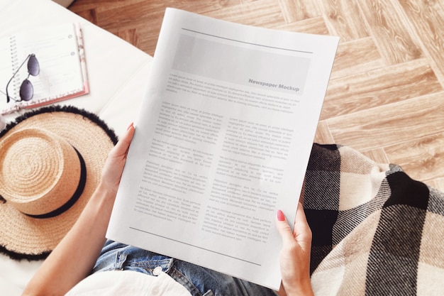 Young woman sitting in living room and reading a newspaper mockup